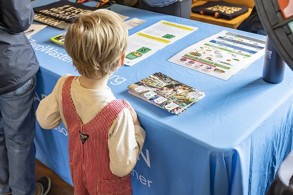 Child in red overalls stands in front of the Zero Waste Marin table looking at flyers