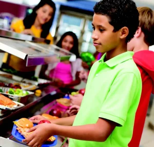 Child in bright green shirt gets lunch in school lunch line