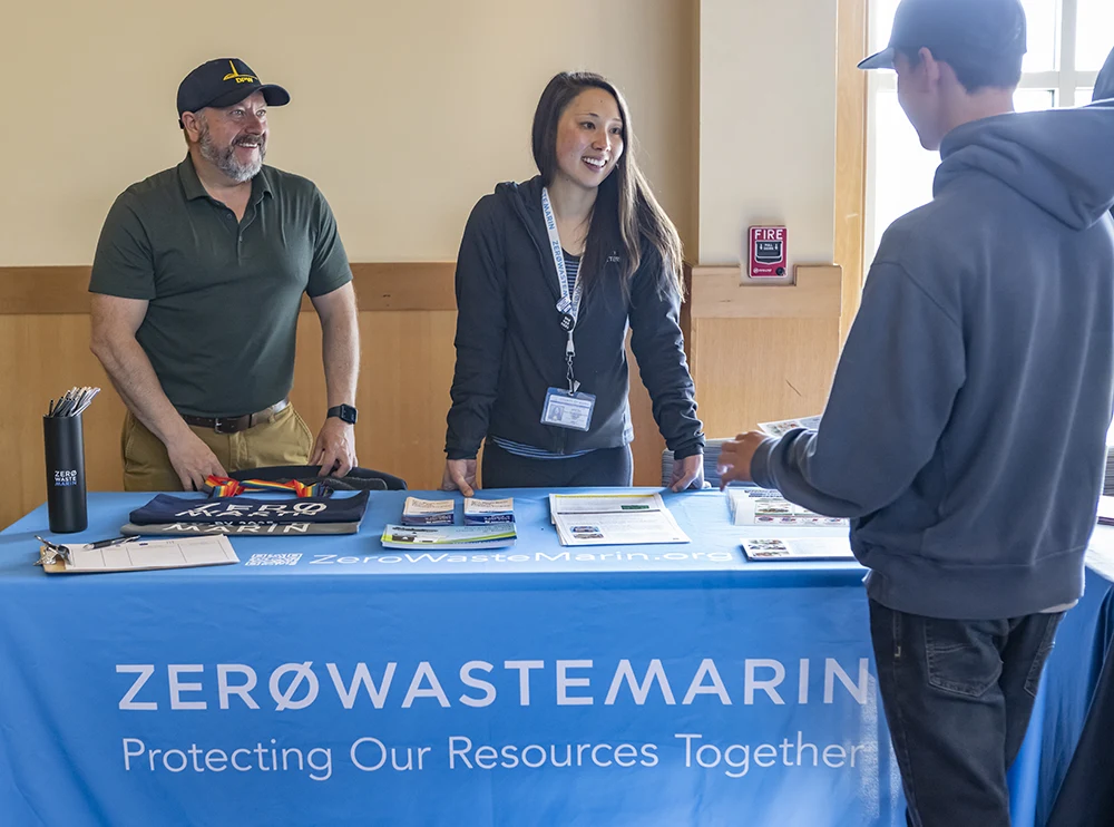 Two Zero Waste coordinators speak with a student at the Zero Waste Marin table at an event in Mill Valley