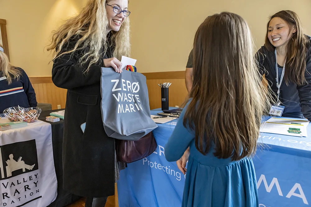 A Zero Waste coordinator presents a reusable bag to a child at a Zero Waste Marin event