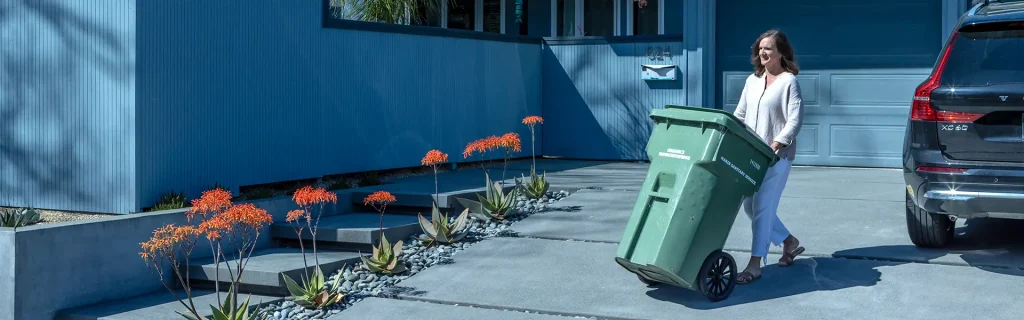 A woman rolls her green organics cart to the curb in front of her home in Marin