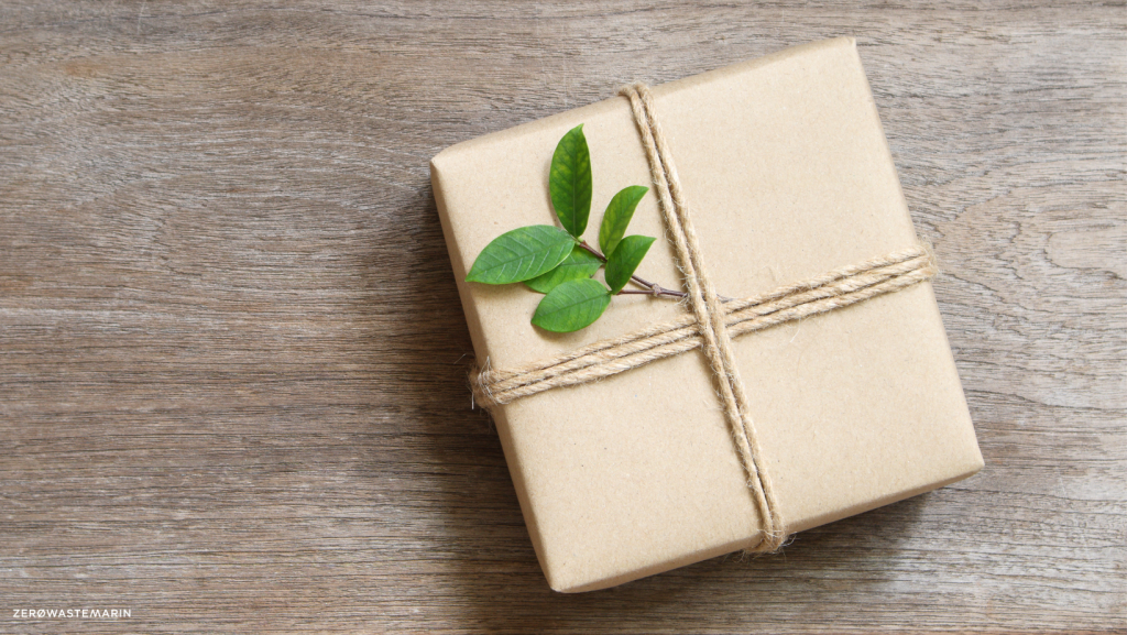 A gift wrapped in plain brown paper with a decoration of natural leaves on a background of wood.
